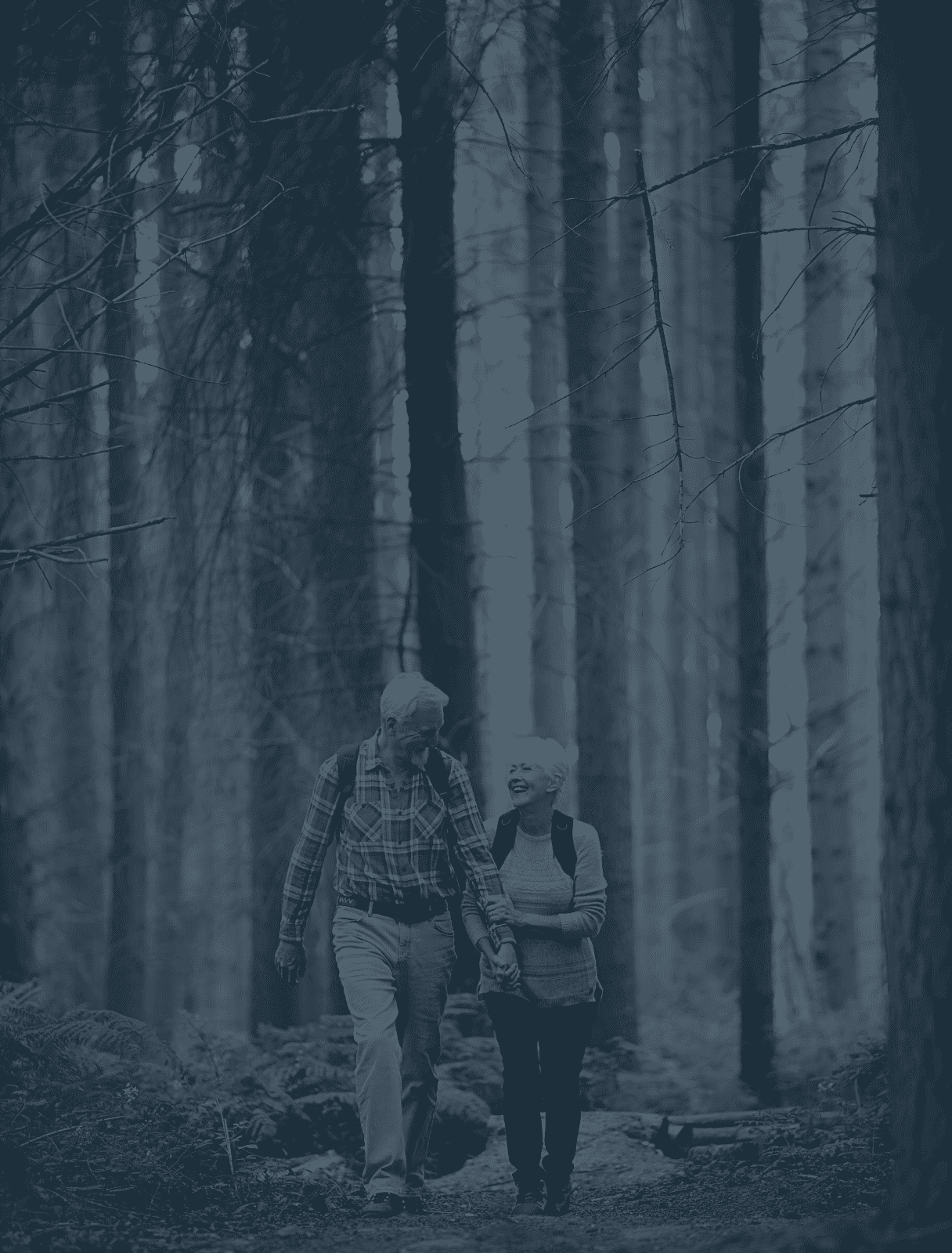Senior couple holding hands while walking through the forest wearing backpacks